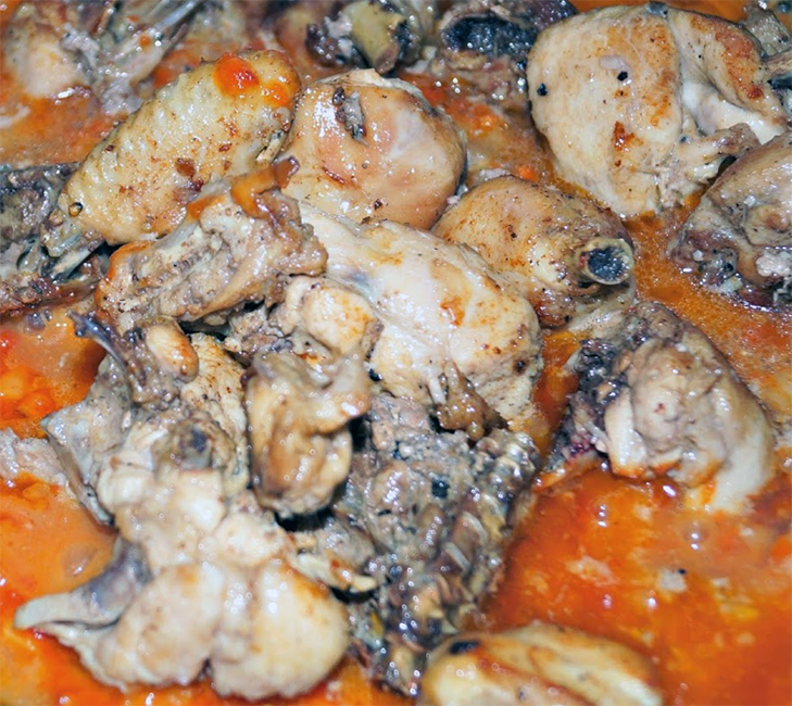 chicken and cassava stew in a tomato and red oil base simmering in a pot