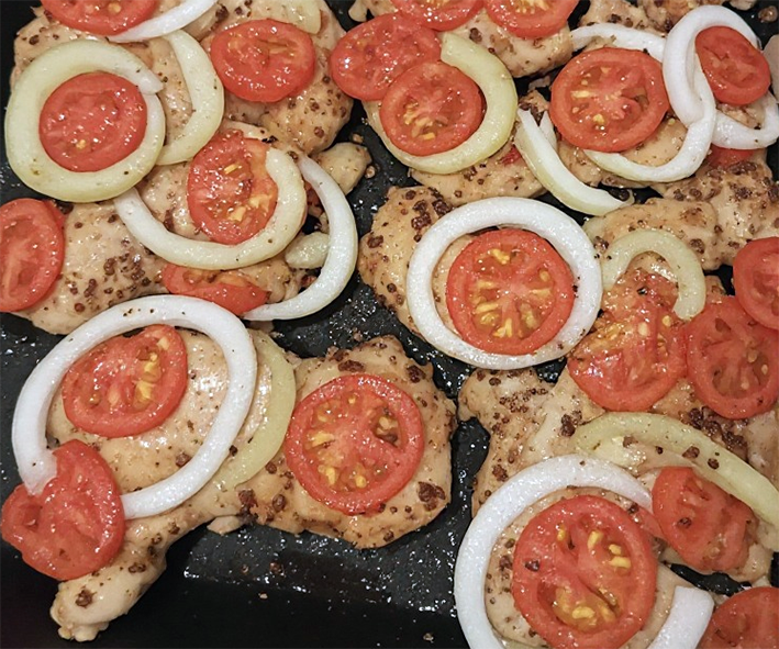 chicken portions is a roasting tin covered with tomato and onion slices