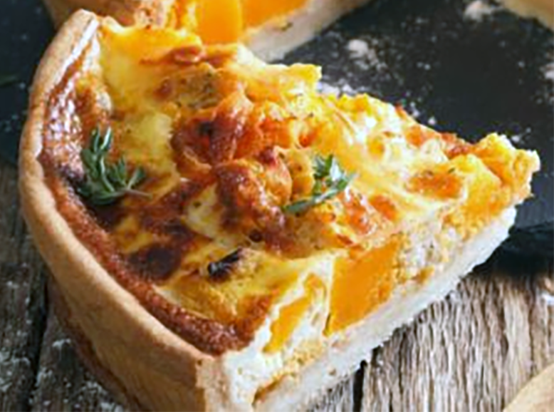 Wedge of pumpkin leek and cheese tart in a herbed pastry crust on a slate