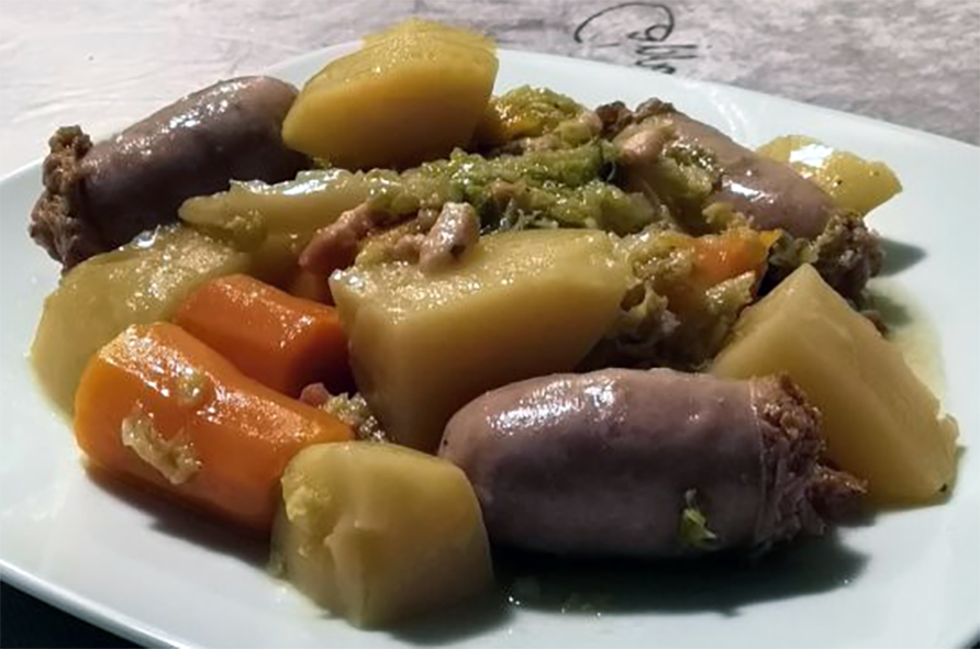 breton ragout of sausages, onion, bacon, cabbage, potatoes and carrots on a white plate