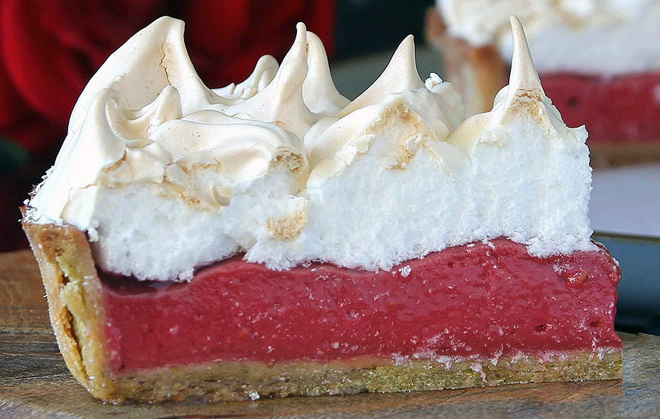 slice of raspberry meringue pie on a wooden chopping board
