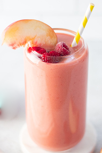 raspberry peach smoothie in a glass topped with raspberries and a peach slice