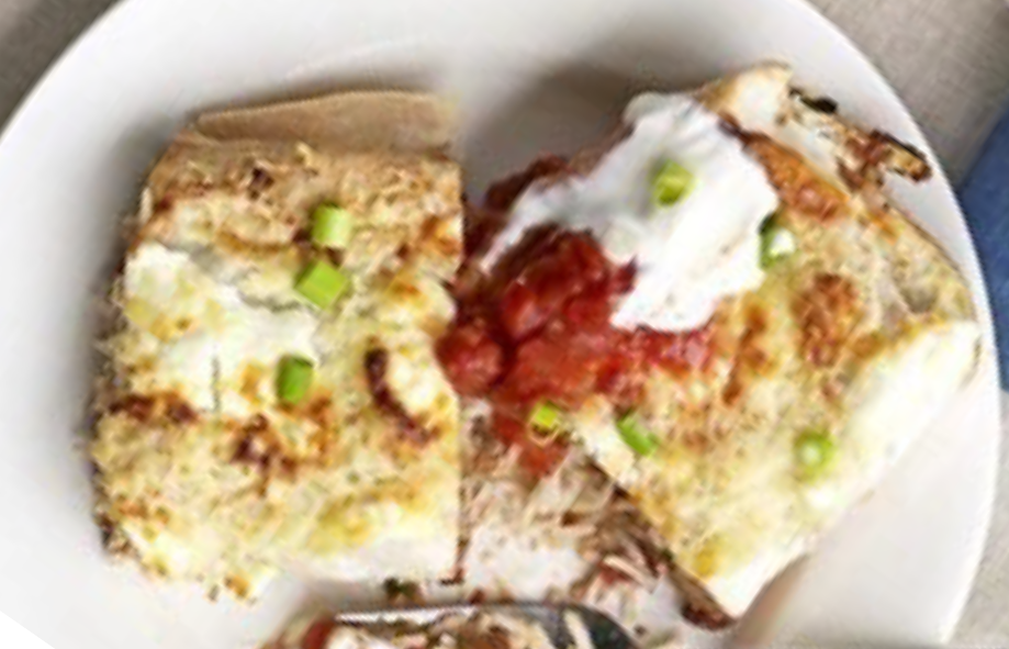 rice and bean filled enchilada served topped with tomato sauce and cheese sauce split open on a plate
