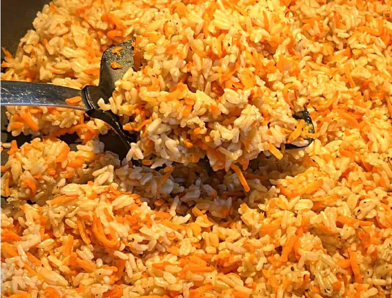 salvadorean carrot rice in a pan lifted with a spoon