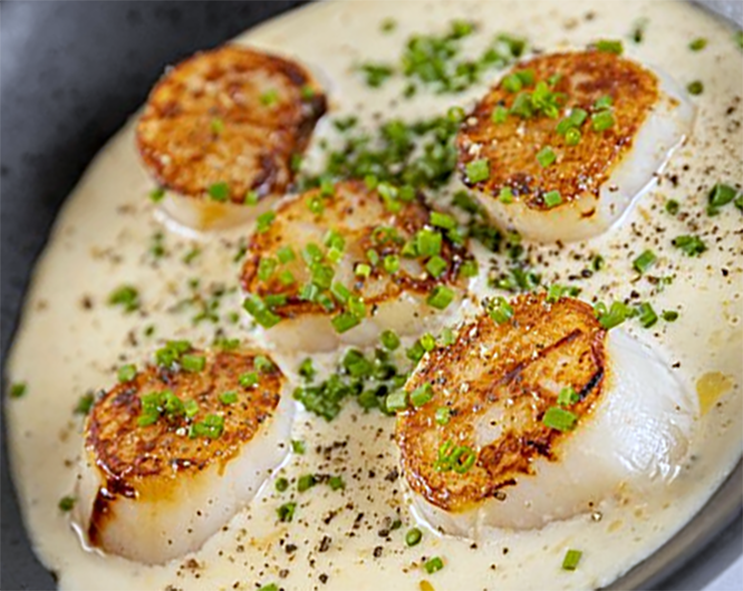 five scallops in an onion cream sauce garnished with chopped parsley