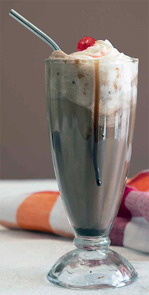 chocolate chip ice cream soda in a tall glass topped with whipped cream and cherry
