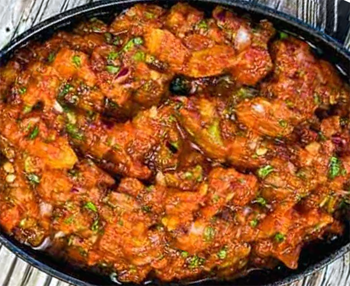 tinned fish fried in a cast iron dish with potatoes, chillies and onion in a tomato base