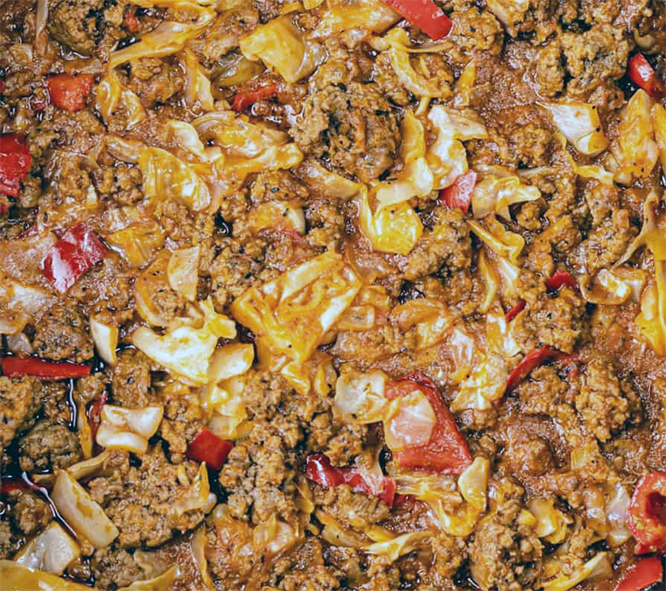 smoorsnoek frying in a pan with cabbage, potatoes and red chillies