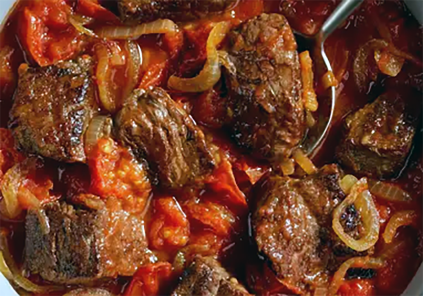 stew of beef in a tomato and onion base with a metal spoon