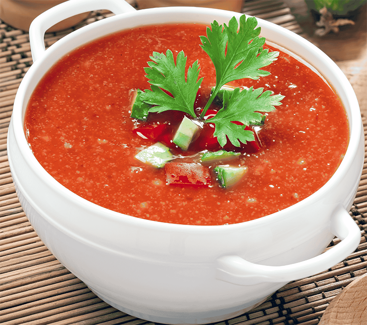 chilled tomato-based Spanish soup served in a bowl garnished with a sprig of flat-leaf parsley and cubes of cucumber