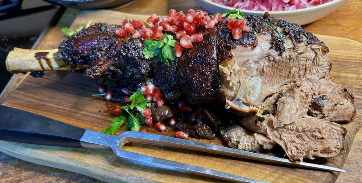 spiced leg of roast mutton with a carving fork served topped with pomegranate arils