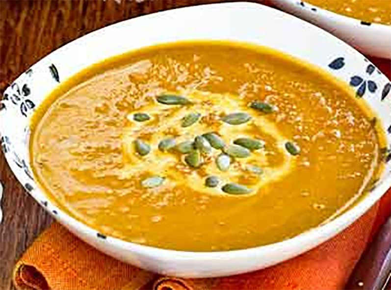 spicy pumpkin soup in a bowl garnished with a swirl of sour cream and pumpkin seeds