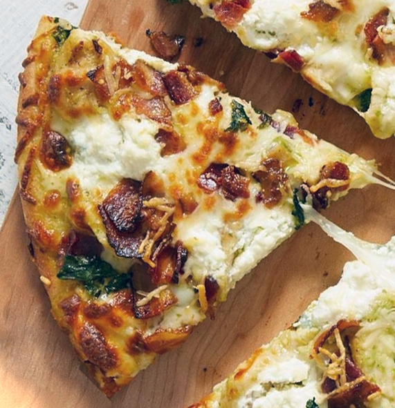 wedge of spinach pesto pizza on a wooden chopping board