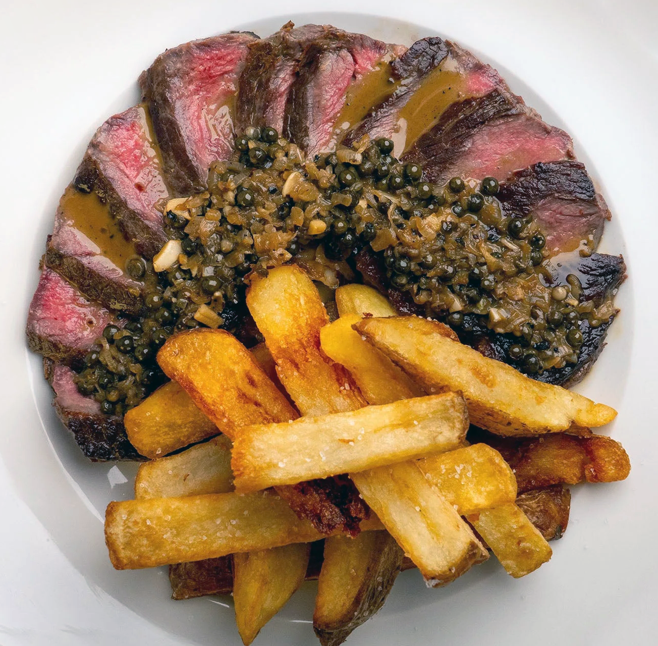 French steak frites, sliced fried been steak served with chips and black pepper sauce on a white plate