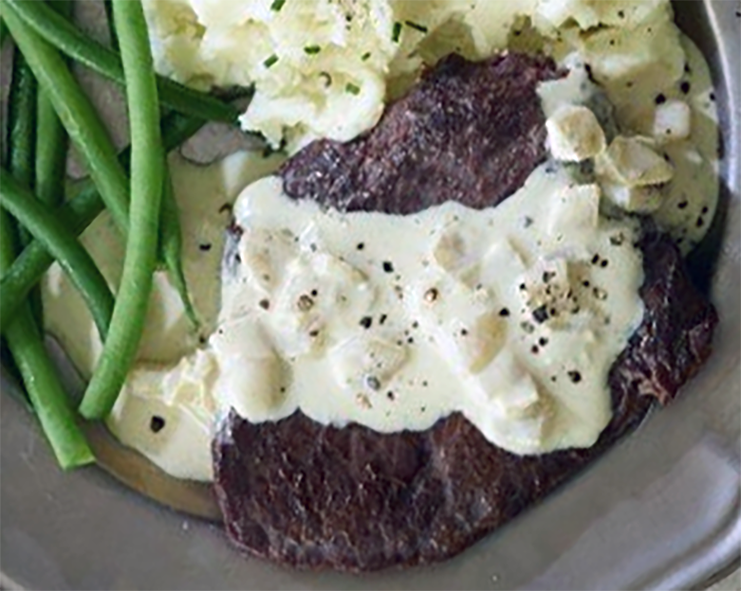ostrich leg steak served with mashed potatoes and green beans with a white cream and white bean sauce