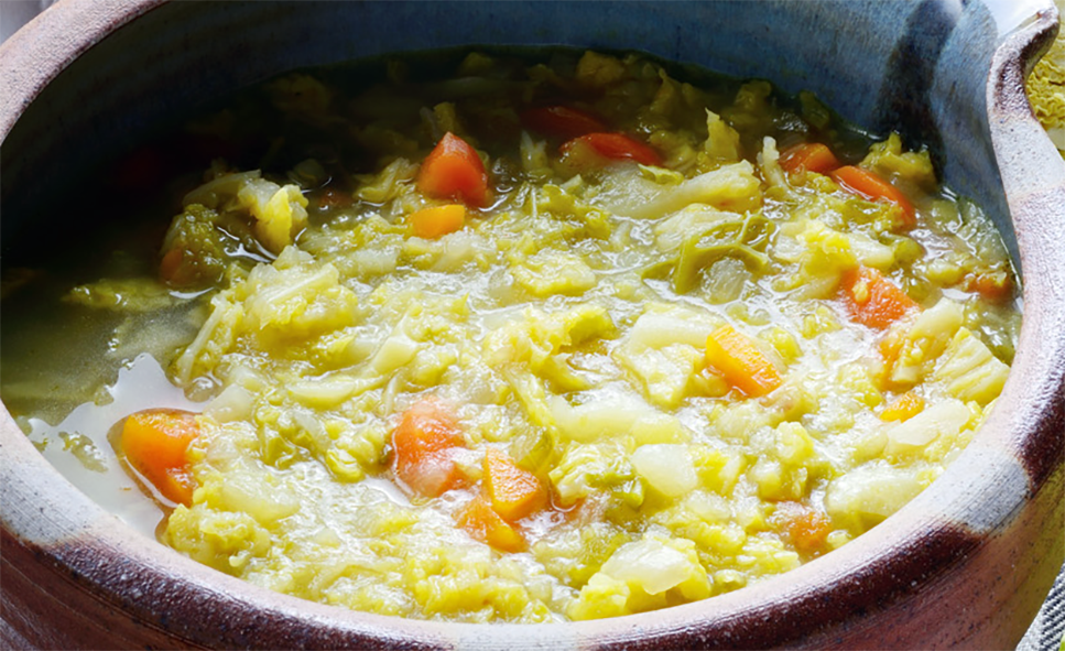 summer soup of lettuce, cabbage, tomatoes, leek, onions, beans, potatoes and peas in a milk base served in an earthenware bowl