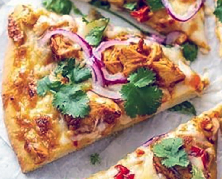 wedge of tandoori chicken pizza garnished with red onion and coriander on a sheet of greaseproof paper