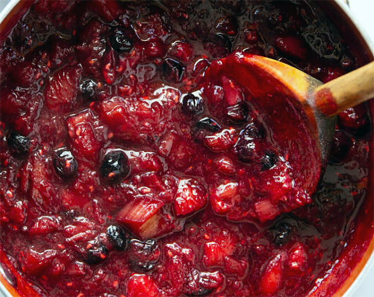 three berries and rhubarb sauce stirred in a pan with a wooden spoon