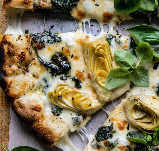wedge of artichoke and three cheese pizza garnished with basil