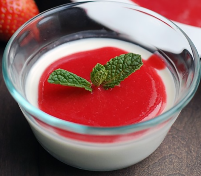 vanilla panna cotta served in a glass bowl topped with a strawberry and raspberry coulis and a sprig of mint