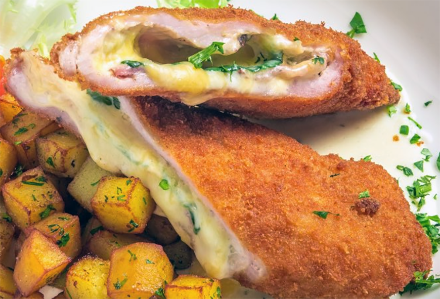 Veal cordon bleu served sliced in half to reveal the cheese and ham filling served with fried potato cubes