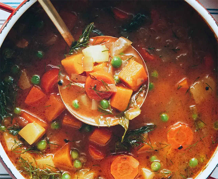 winter vegetable soup lifted from a stockpot with a ladle
