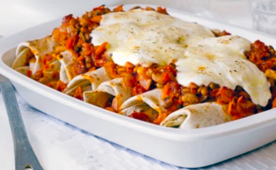 vegetarian enchiladas with a bean chili filling topped with more bean chili and a yoghurt and cheese blend in a white baking dish
