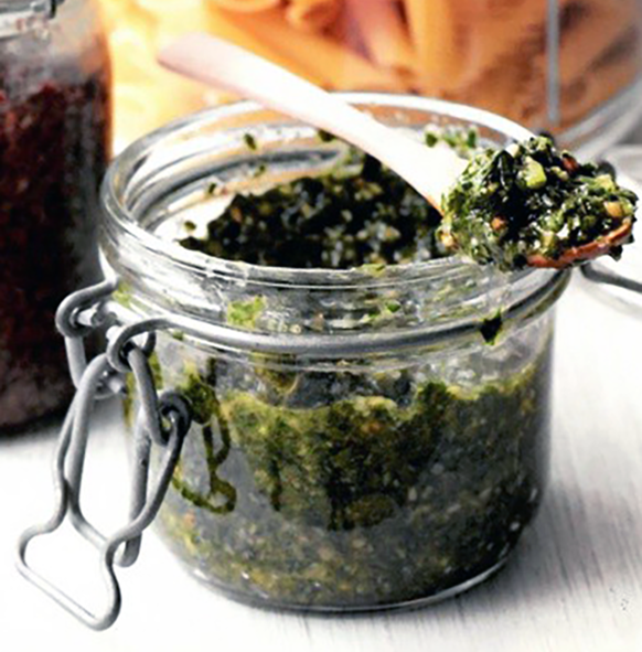 wild garlic and wild mustard greens pesto in a clip top jar with a portion on a wooden spoon
