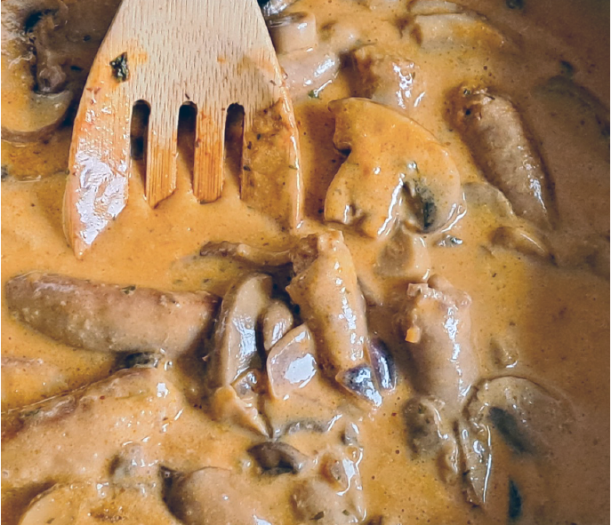 sausage and mushrooms in a cream sauce stirred with a wooden spatula