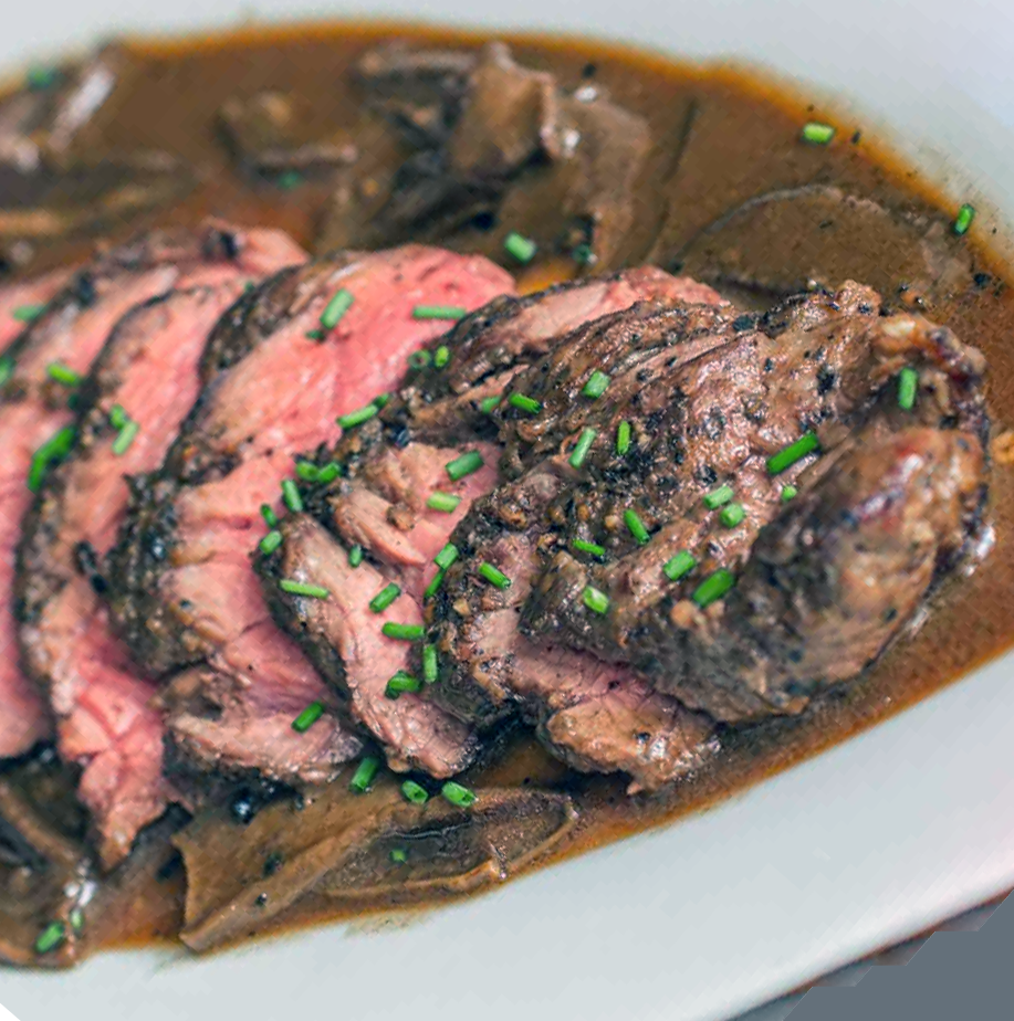sliced beef steak with a mixed wild mushrooms sauce served on a plate with a chive garnish