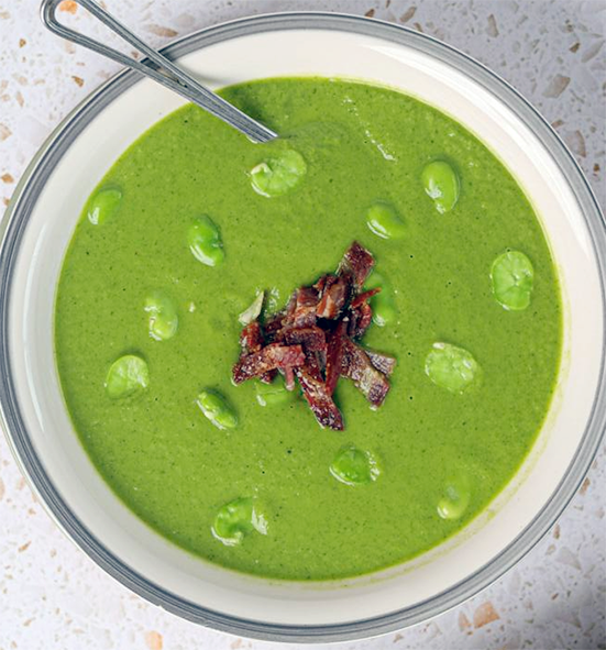 broad bean soup served in a bowl with a garnish of baby broad beans and crisp-fried bacon