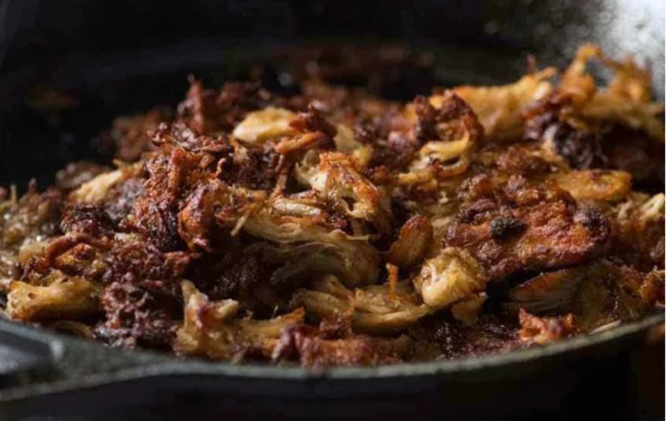carnitas or mexican pulled pork frying down in a cast iron casserole