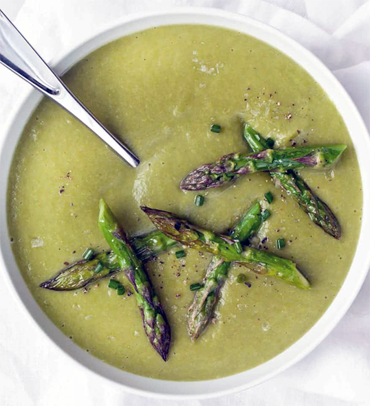 chilled asparagus soup served in a bowl with a spoon and a garnish of asparagus heads