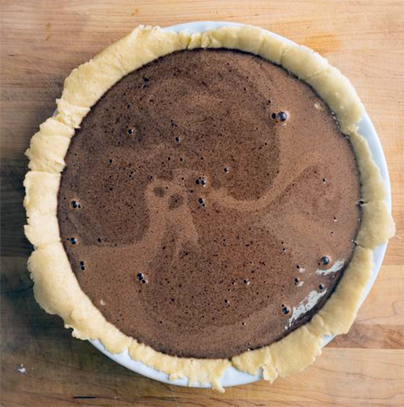 chocolate orange flan in a metal tin cooling on a wooden chopping board