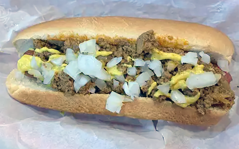 hot dog in a hot dog bun topped with meat relish, yellow mustard and diced onion