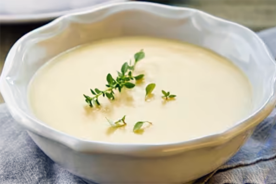 cream of potato soup served in a bowl and garnished with a sprig of thyme