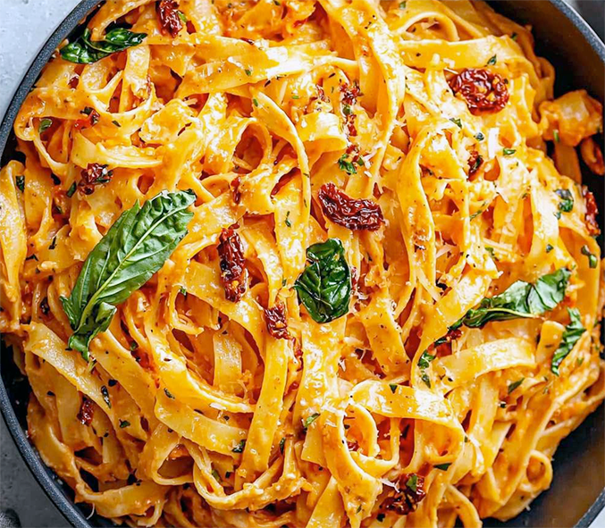 fettuchine pasta tossed with a sun-dried tomato sauce and garnished with basil in a metal dish