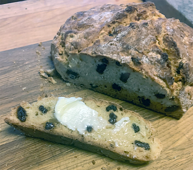 fruited soda bread on a wooden chopping board with a slice cut off and buttered
