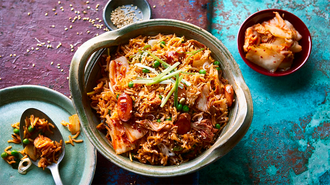 bowl of kimchi fried rice with spoon on a plate and a small bowl of kimchi