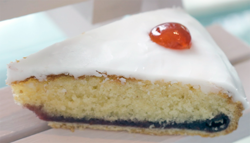 slice of iced/glazed bakewell tart on a white bench