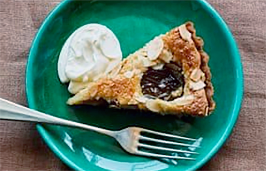 wedge of greengage and almond tart served with a fork and a dollop of cream