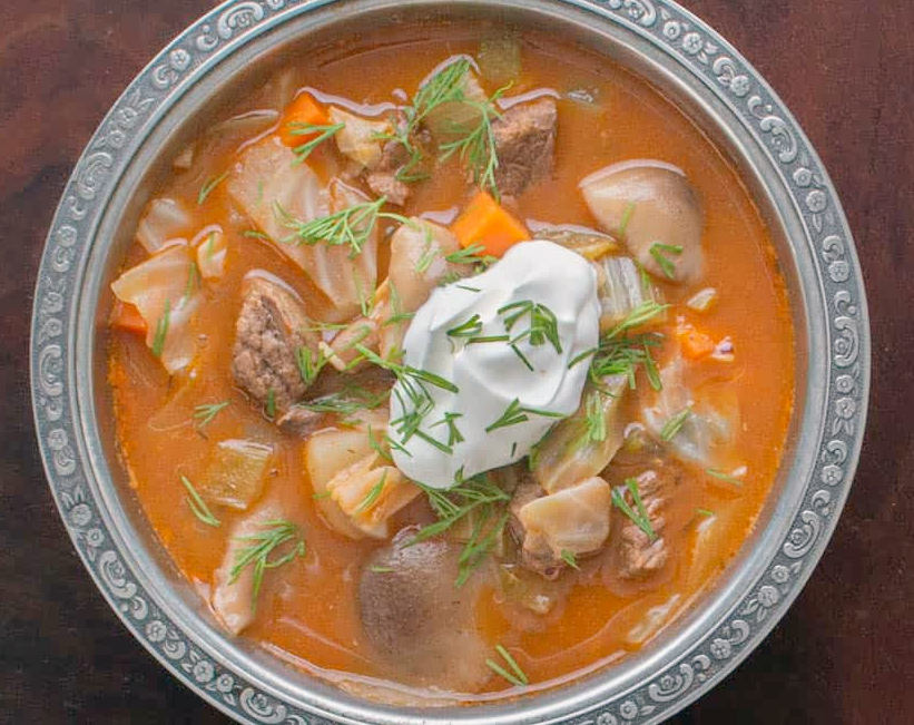 hot and sour soup of venison and honey fungus in a paprika base served in a bowl with dill and sour cream garnish