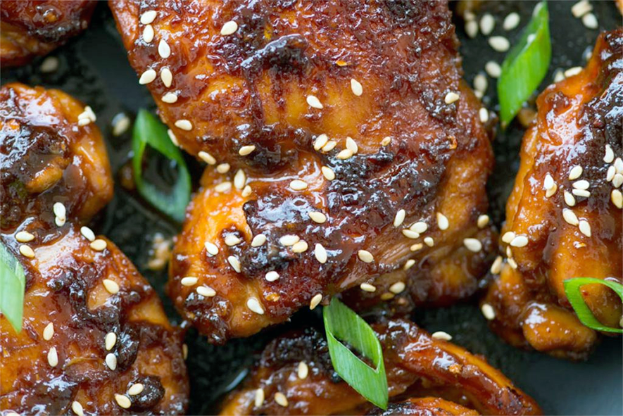 hot and sticky chicken thighs shown garnished with spring onion greens and sesame seeds