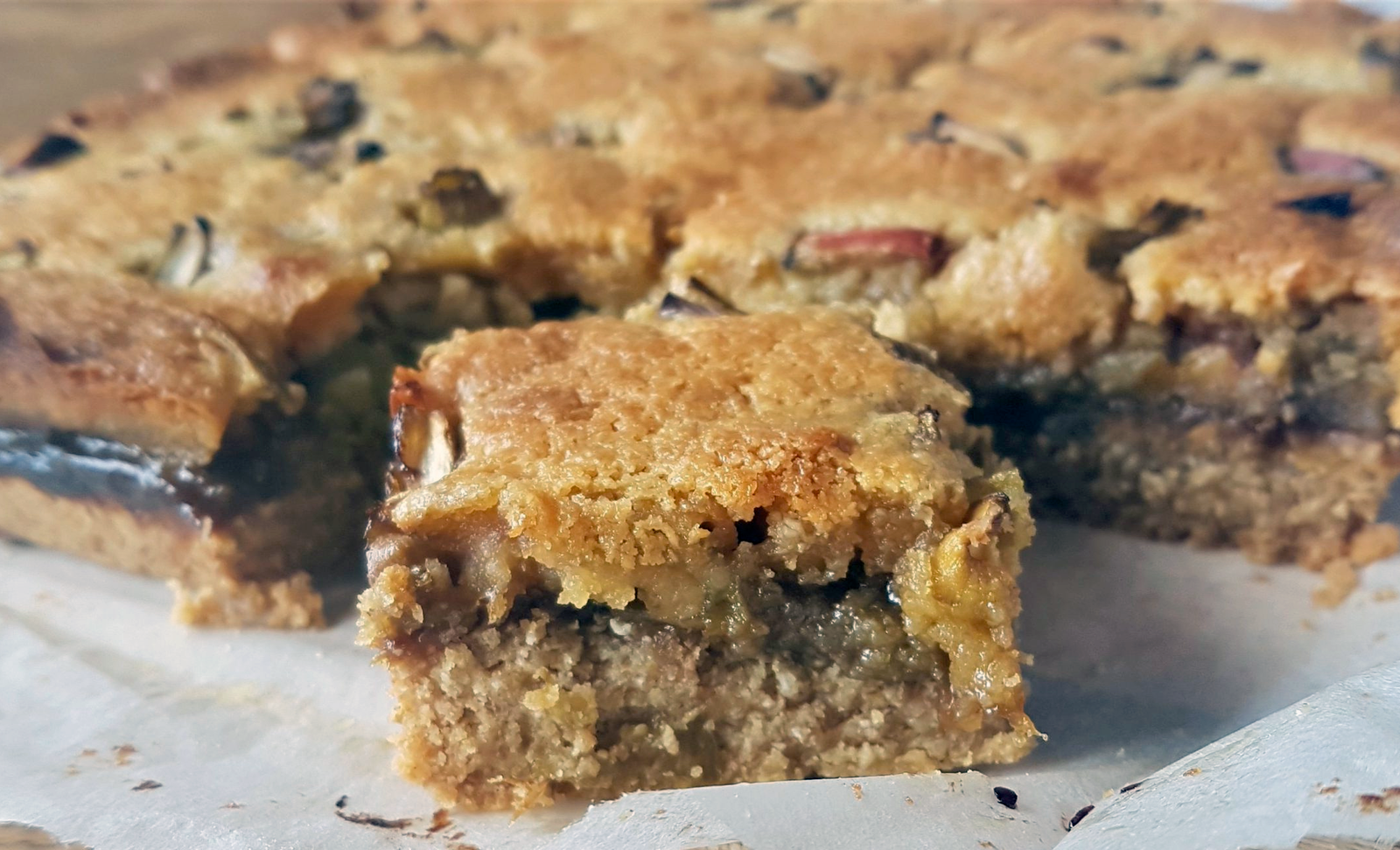 slices of japanese knotweed frangipane tart with a pastry base, knotweed jam filling and frangipane topping studded with knotweed pieces on a sheet of greaseproof paper