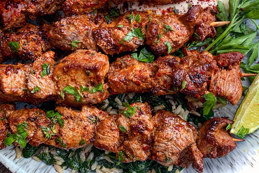 skewers of lamb sis kebab arranged on a plate with flat-leaf parsley and a wedge of lime
