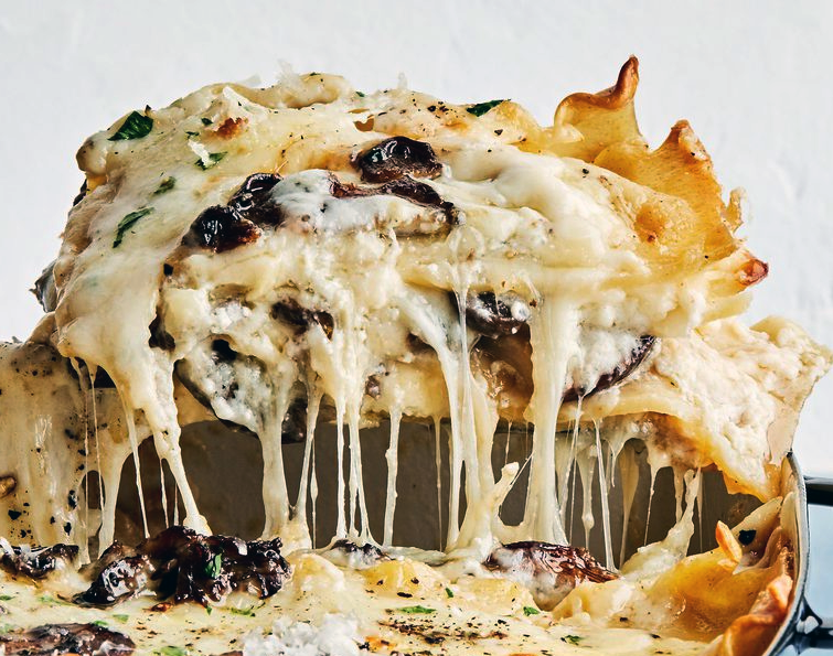 square of lasagne with mushrooms and cheeses being lifted from a baking dish