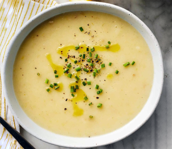 leek and potato soup with avocado leaf served in a white bowl with a garnish of olive oil, cracked black pepper and chives