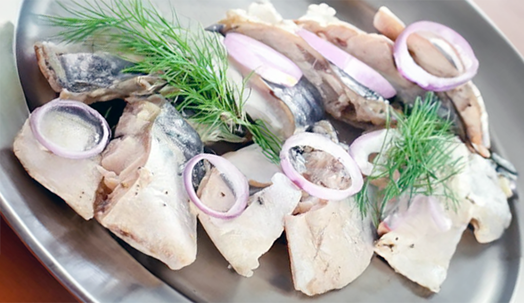 baked marinated mackerel served sliced on a metal plate with a garnish of red onion rings and dill sprigs