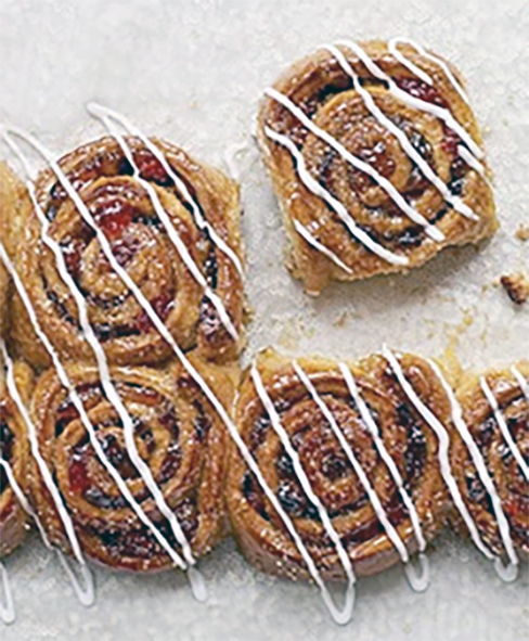 spiral mincemeat chelsea buns drizzled with white icing on a white tablecloth