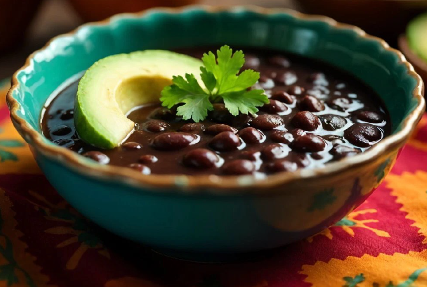 Oaxacan black beans with avocado leaf served in a blue bowl with a garnish of flat-leaf parsley and a slice of avocado